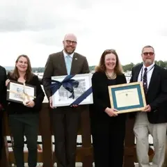 Dignitaries and Museum leadership stand aboard Mayflower II holiding commemorative objects.