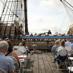 Seated guests enjoy remarks delivered from aboard Mayflower II.