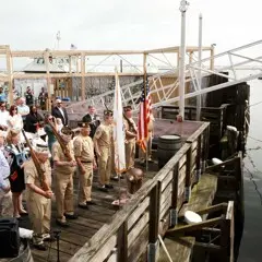 Veterans and guests stand for pledge of allegiance on dock at Mayflower II.