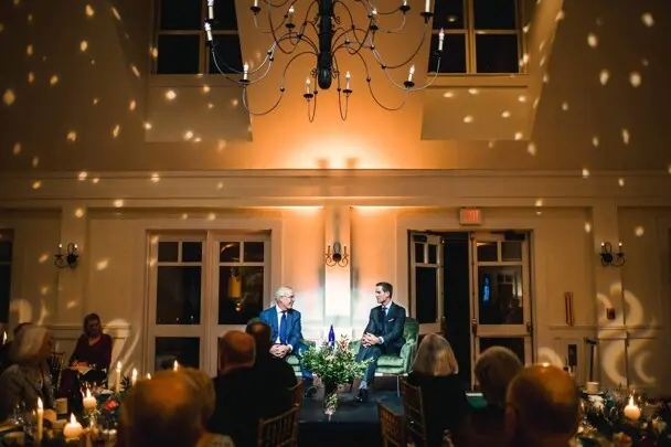 Jared Bowen and David Brooks in conversation in stage while event attendees dine.