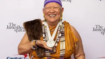 Sherry Pocknett dressed in regalia holds James Beard award.
