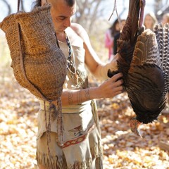 Museum educator in regalia examines turkey on the Historic Patuxet Homesite.