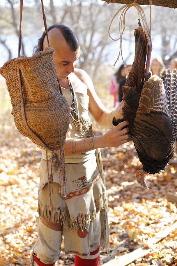 Museum educator in regalia examines turkey on the Historic Patuxet Homesite.