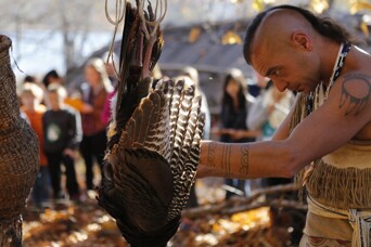 Museum educator in regalia plucks turkey on Historic Patuxet Homesite.