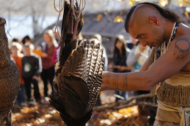 Museum educator in regalia plucks turkey on Historic Patuxet Homesite.