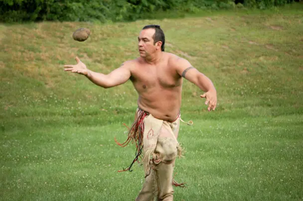 Wampanoag man dressed in regalia plays sports in a grassy field