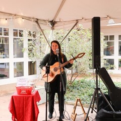 Musician Abby Vail plays guitar and sings in tented courtyard.