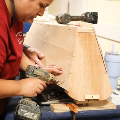 A woman demonstrates how to make a wooden boat model.