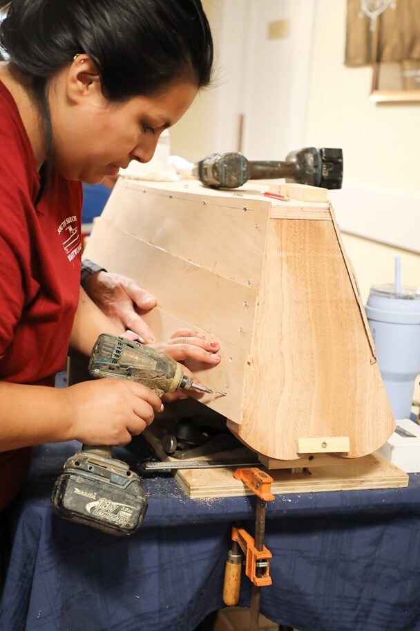 A woman demonstrates how to make a wooden boat model.