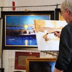 Artist Vincent Crotty paints on a canvas while surrounded by his finished paintings.