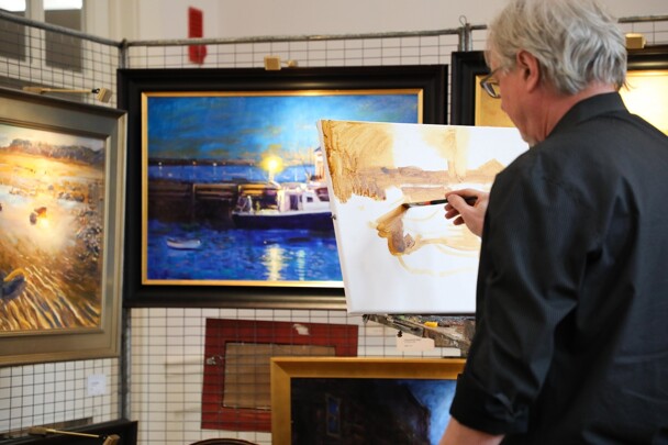 Artist Vincent Crotty paints on a canvas while surrounded by his finished paintings.