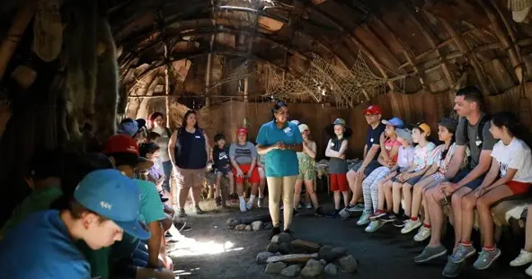 Museum Educator stands in center of wetu and talks to seated guests.