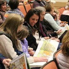 A family in the Lynn Theater read a Jan Brett book.