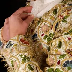 A woman modeling the Plimoth Jacket raises her hands to her white, lace collar.