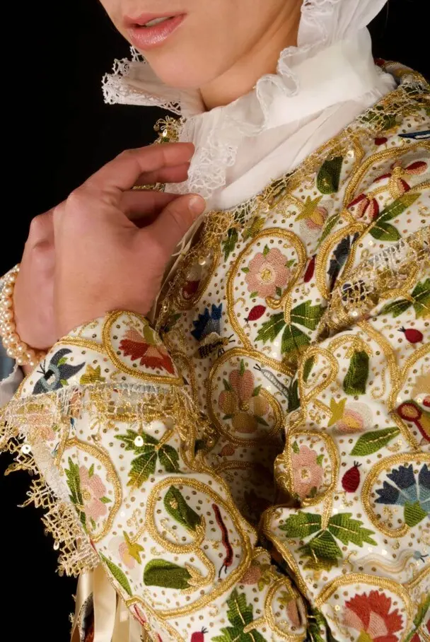 A woman modeling the Plimoth Jacket raises her hands to her white, lace collar.