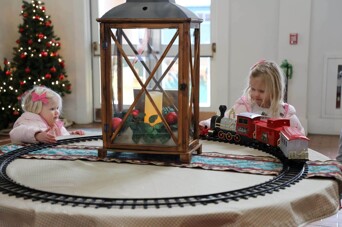 Two girls watch a toy train in motion.