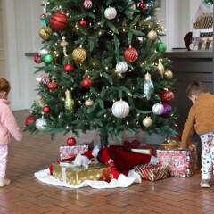 Two children examine wrapped presents underneath a Christmas Tree.