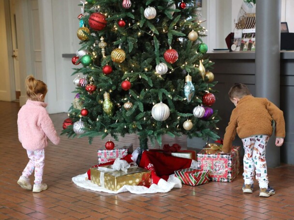 Two children examine wrapped presents underneath a Christmas Tree.
