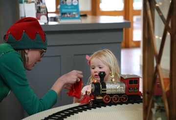 Santa's elf gifts a red velvet bag to a child containing a magical bell.