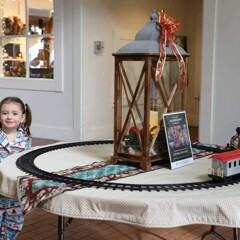 Girl stands near a toy train in motion.