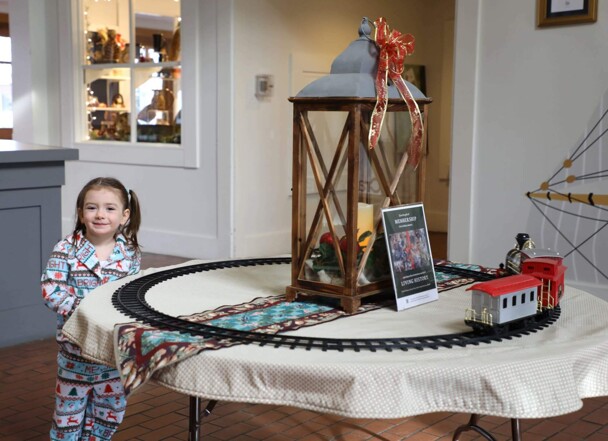 Girl stands near a toy train in motion.