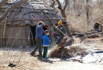 Volunteers rake leaves and twigs in front of wetu on the Historic Patuxet Homesite.