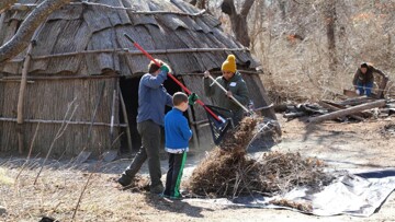 Volunteers rake leaves and twigs in front of wetu on the Historic Patuxet Homesite.
