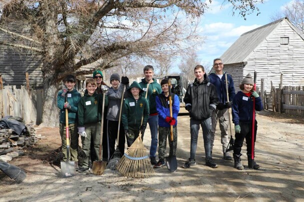 A group of boy scouts stand together holding rakes and shovels in the 17th-Century English Village.