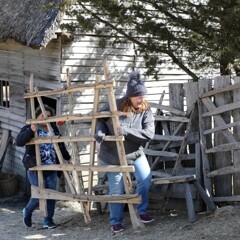 Two volunteers carry a wooden fence panel in the 17th-Century English Village.