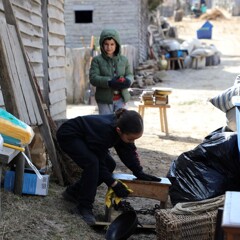 A young girl polishes wooden furniture in front of a Pilgrim house as another young volunteer looks on.