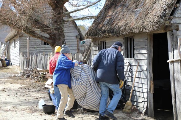 Volunteers work together to carry a mattress inside of a Pilgrim house.