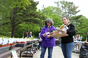 Two women at the plant sale, one looking at a list, the other holding a box of seedlings