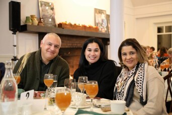 Three guests seated at Thanksgiving table with glasses of apple cider