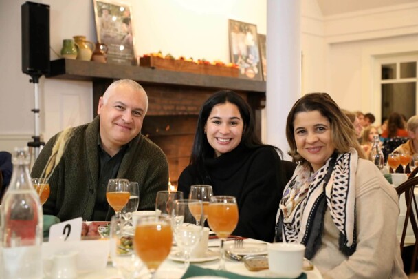 Three guests seated at Thanksgiving table with glasses of apple cider