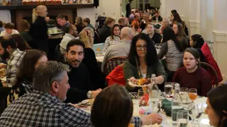 Guests sit at round tables with white tablecloths enjoying Thanksgiving dinner.