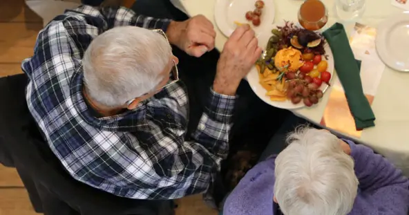 A couple eats a plate of cheese and fruit at set table.