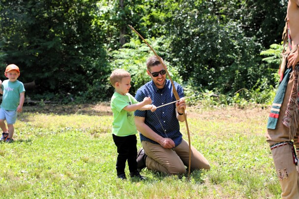A father helps his son learn archery on the Historic Patuxet Homesite.