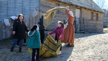 Two young girls and their mother help a Pilgrim woman with laundry in Plymouth Colony.