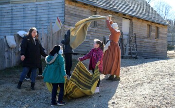 Two young girls and their mother help a Pilgrim woman with laundry in Plymouth Colony.
