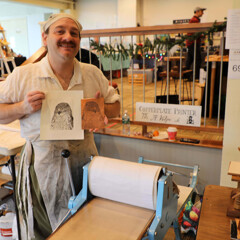 Artisan in historic dress holds up print he has created using historic methods