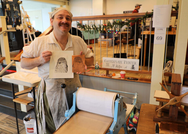 Artisan in historic dress holds up print he has created using historic methods