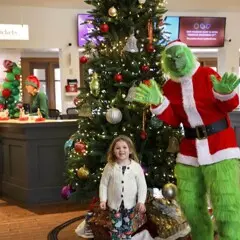 Child poses in front of a decorated Christmas tree with the Grinch
