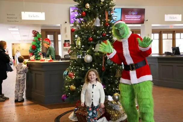 Child poses in front of a decorated Christmas tree with the Grinch
