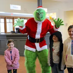 Three children pose with the Grinch in Plimoth Patuxet's museum lobby.