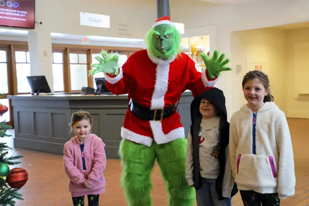 Three children pose with the Grinch in Plimoth Patuxet's museum lobby.