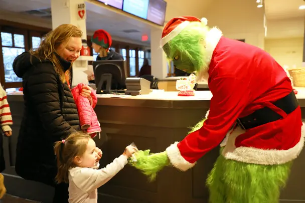 The Grinch gives a young girl a candy cane.