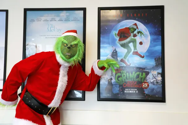 The Grinch poses with his own framed movie poster.
