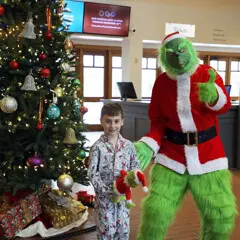 Grinch poses with boy attending the matinee dressed in pajamas in front of a decorated Christmas tree.