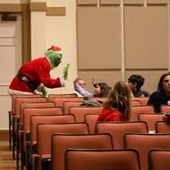 The Grinch high-fives children seated in a movie theater.