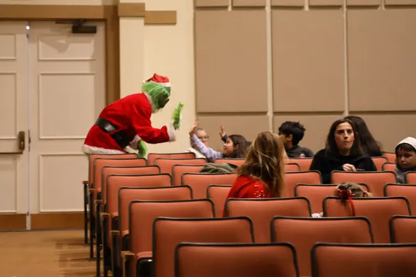 The Grinch high-fives children seated in a movie theater.